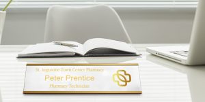 Building trust with a white metal name plate with gold engraving of a logo, name and title sitting on a desk.